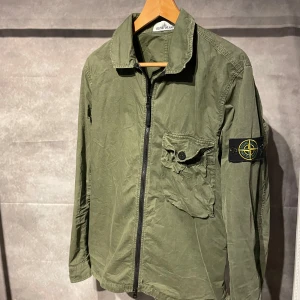 Stone Island Overshirt  - Snygg grön jacka från Stone Island med dragkedja och en ficka på bröstet. Jackan har en ikonisk patch på ärmen och är perfekt för en stilren look.
