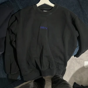 Svart sweatshirt från Vailent - Säljer en svart sweatshirt från Vailent med trycket 'IGNITE' i blått framtill och ett stort färgglatt tryck av en vulkan på baksidan. Tröjan har långa ärmar och ribbade muddar vid ärmslut och nederkant. Perfekt för en cool och avslappnad stil.