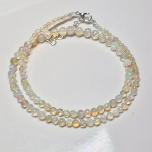 Halsband med opalpärlor - Elegant halsband med skimrande opalpärlor i olika nyanser. Pärlorna är runda och reflekterar ljus vackert, vilket ger en regnbågseffekt. Halsbandet har ett klassiskt lås i silverfärg. Perfekt för att ge en touch av glamour till din stil.