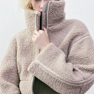 Beige teddyjacka med dragkedja - Mysig beige teddyjacka med hög krage och dragkedja framtill. Jackan har en avslappnad passform och långa ärmar. Storlek M men sitter som en S!