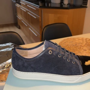 Mocka skor med Lack - Snygga svarta sneakers med en kombination av mocka och lackdetaljer. Skorna har en vit sula och snörning framtill. Perfekta för en stilren look.