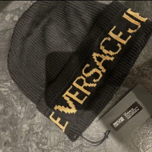 Svart mössa från Versace Jeans Couture - Snygg svart mössa från Versace Jeans Couture med guldig text längs kanten. Köpt från Zalando, helt ny aldrig använd 550kr