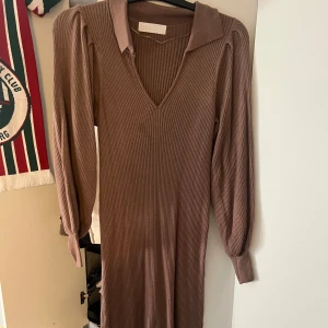 Brun ribbad klänning  - Snygg brun ribbad klänning med v-ringning och långa ärmar. Perfekt för en stilren look med en bekväm passform. Klänningen har en klassisk design som passar till många tillfällen. Har lite fläckar som jag inte försökt få bort men annars i fint skick!