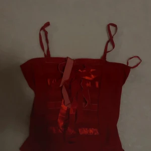 Röd korsettopp med rosett - Super unique and beautiful vintage top. Never worn by me. Sits tight on the body and has stretch. No size written on it but it fits me who is a size S!