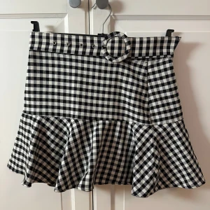 Rutig kjol med volang från Zara - Snygg svartvit rutig kjol från Zara med volangdetalj och ett matchande bälte. Inbyggda shorts i samma mönster och material. Storlek M, men passar S om man använder bältet! Så fin!