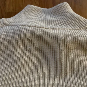 Vintage Beige stickad tröja/ Maison Margiela - Säljer en stilren vintage beige stickad tröja från Maison Margiela. Tröjan har en dragkedja framtill och är långärmad med ribbade detaljer. Perfekt för en avslappnad och trendig look. Tillverkad i Italien.