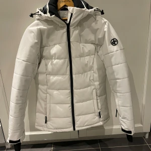 Vit skidjacka - Figursydd vit skidjacka från crossportswear. Knappt använd. Håller värme bra i backen och är väldigt snygg. Liftkorts ficka och luvan går över hjälmen!
