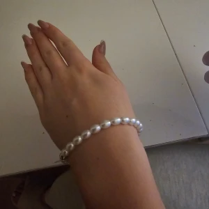 Pärlarmband med gulddetalj - Elegant pärlarmband med vita pärlor och en gulddetalj. Perfekt för att ge en klassisk touch till din stil. Armbandet är elastiskt men åt det större hållet från grunden.