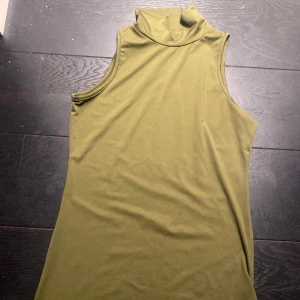 Olivgrön ärmlös polotopp - Snygg olivgrön ärmlös polotopp i mjukt material. Perfekt för lager-på-lager eller som den är. Enkel och stilren design som passar till många olika outfits.