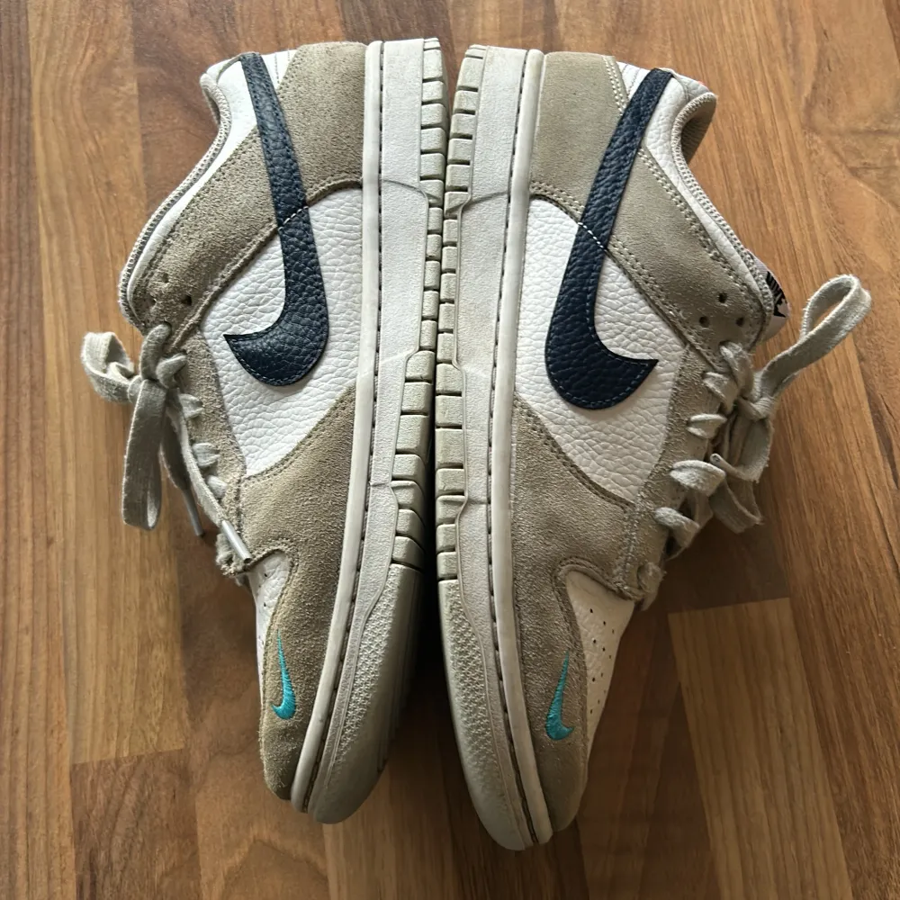 Säljer ett par Nike Dunk sneakers i en snygg kombination av beige mocka och vit skinn. Skorna har en klassisk design med svarta och turkosa detaljer, inklusive den ikoniska Nike-loggan på sidan. De är i bra skick med lite slitage på sulorna. Perfekta för både vardag och fest!. Skor.