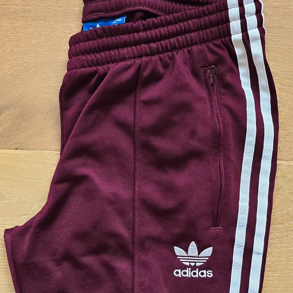 Ännu ett par Adidas Track Pants-byxor i min samling som förtjänar att nyttjas vidare och oftare!  Dessa supercoola i burgundy-färg är sjukt snygga att matcha mellan olika stilar.  Färg: Burgundy/vinröd/lilaröda  Midja: 38 cm (medium) med stretch och . Jeans & Byxor.