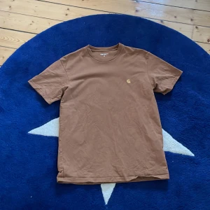 Brun Carhartt-T-shirt  - Carhartt t-shirt med tryck på bröstet. Tröjan är i gott skick och ordinarie pris var 499kr