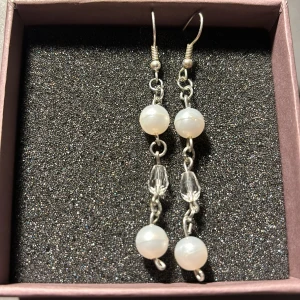 Silverörhängen med pärlor - Säljer ett par eleganta silverörhängen med vita pärlor och klara kristaller. De har en hängande design med två pärlor och en kristall emellan, vilket ger en stilren och klassisk look. Perfekta för både vardag och fest!⚜️🤍