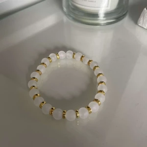 Vitt armband med gulddetaljer - Snyggt och stilrent armband med vita pärlor och guldfärgade detaljer. Perfekt för att ge en elegant touch till vilken outfit som helst. Passar både till vardags och fest!