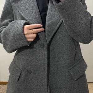 Grå ullkappa - Säljer en stilren grå ullkappa som är perfekt för höst och vinter. Den har en klassisk design med dubbelknäppning och stora slag. Kappan är långärmad och har praktiska fickor framtill. Den är i bra skick och passar både till vardags och lite finare tillfällen.