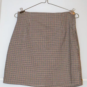 Rutig kjol från H&M - Snygg rutig kjol från H&M i klassiskt hundtandsmönster. Perfekt för både vardag och fest! Kjolen har en stilren design och är i mycket bra skick. Passar utmärkt till höst- och vintergarderoben.