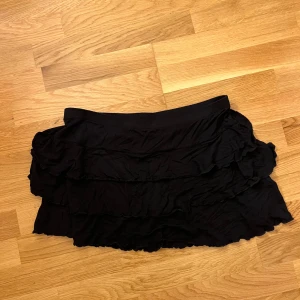 Svart volangkjol från Gina Tricot - Säljer en superfin svart volangkjol från Gina Tricot i storlek L. Kjolen har flera lager av volanger som ger en härlig och lekfull look. Perfekt för både vardag och fest! 🖤