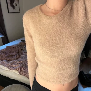 Beige fluffig tröja med öppen rygg - Säljer en supermjuk och fluffig beige tröja med en snygg öppen rygg och knytband. Perfekt för både mysiga hemmakvällar och att klä upp för en utekväll. Tröjan är croppad och har långa ärmar. Passar perfekt till höst och vår!