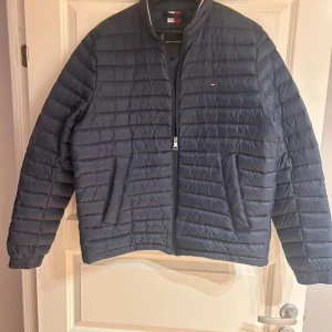 Mörkblå quiltad jacka från Tommy Hilfiger - Säljer en snygg mörkblå quiltad jacka från Tommy Hilfiger i storlek L. Jackan har en dragkedja framtill och är perfekt för höst och vår. Den är i mycket bra skick och har en stilren design med det klassiska Hilfiger-emblemet på bröstet.