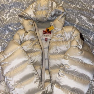 Beige pufferjacka från Parajumpers - Säljer en snygg beige pufferjacka från Parajumpers i mycket bra skick. Jackan har en glansig finish och är perfekt för kalla dagar. Den har en huva och dragkedja framtill, samt ribbstickade muddar vid ärmsluten. Märkeslogga på ärmen ger en extra touch och är perfekt för dom kalla dagarna under vintern!! Skriv och ställ gärna frågor. Pris kan diskuteras 
