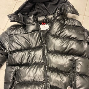 Svart pufferjacka från Moncler - Säljer en snygg svart pufferjacka från Moncler i mycket bra skick. Jackan har en glansig finish och är perfekt för kalla dagar. Den har en dragkedja framtill och praktiska fickor med dragkedjor. Perfekt för vintern och hösten!