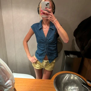 Blå jeansblus - Snygg blå jeansblus i tight passform med korta ärmar och knappar framtill. Perfekt för sommardagar eller en avslappnad utekväll. Blusen har en stilren design med en lätt rynkad detalj vid bysten. Använd 3 gånger!