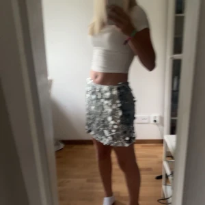 Glittrig paljettkjol - Säljer en superglittrig kortkjol täckt med silverpaljetter. Perfekt för nyårsfesten eller en utekväll när du vill glänsa! Kjolen har en tight passform och är i mycket bra skick. Den är gjord av polyester och har en bekväm resår i midjan.