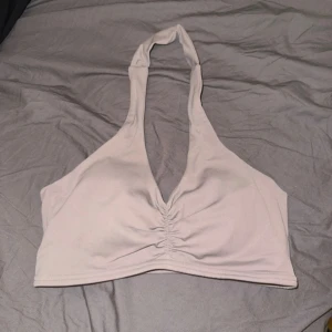 brun beige halterneck topp - Säljer en snygg brun beige halterneck topp i mjukt material. Toppen har en rynkad detalj framtill och är perfekt för träning eller en utekväll. Den är bekväm och stilren, lätt att matcha med olika outfits.