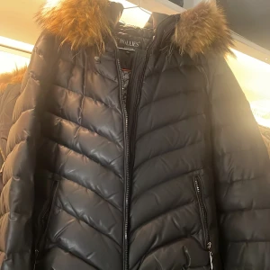 Svart dunjacka med äkta päls från Hollies - Säljer en snygg svart dunjacka från Hollies med en fluffig äkta päls på huvan. Jackan saknar  dragkedjan framtill men den går att fixa enkelt hos en skräddare. Den är både stilren och varm, vilket gör den till ett måste i garderoben. Passar perfekt för vinterns alla äventyr! 🖤