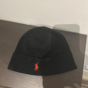 Svart mössa från Polo Ralph Lauren - Snygg svart mössa från Polo Ralph Lauren med röd broderad logga framtill. Använt 2 gånger och väljer att sälja eftersom jag inte passar i mössa, nypris 500kr