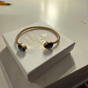 Guldarmband med blå stenar från Caroline Svedbom - Säljer ett elegant guldarmband från Caroline Svedbom med två stora blå stenar 🩵