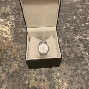 Gucci Klocka - Hej! Säljer en elegant silverfärgad klocka från Gucci i originalförpackning. Klockan har en stilren design med ett klassiskt armband i metall och en vit urtavla med bronsiga detaljer. Perfekt för både vardag och fest 🎈 . Kommer med originalbox och dokumentation till kommer även extra länkar. Nypris på denna klocka är 8 tusen!Den tickar inte just nu, men behövs byta batteri! Kontakta vid frågor och funderingar! Mvh carusfashion 