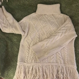 Beige stickad polotröja med fransar - Superfin beige stickad polotröja från Zara i storlek L men passa också än M bra med flätmönster och långa ärmar. Den har en mysig polokrage och coola fransar längst ner som ger en unik touch. Perfekt för kalla dagar när du vill vara både varm och stilren. Passar perfekt till jeans eller leggings!