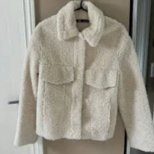 Vit teddyjacka - Supermysig vit teddyjacka i mycket bra skick. Perfekt för höst och vinter med sin fluffiga och varma design. Jackan har långa ärmar och praktiska fickor framtill. Den stängs med knappar och har en klassisk krage. Perfekt för att hålla sig varm och stilren under kyliga dagar🤍🤍!