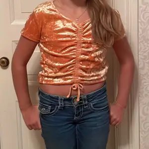 Säljer en superfin orange sammetstopp med korta ärmar. Toppen har en snygg knytdetalj framtill som ger en cool look. Perfekt för sommarens fester eller en dag på stan. Den är i bra skick och passar perfekt till jeans eller kjol.