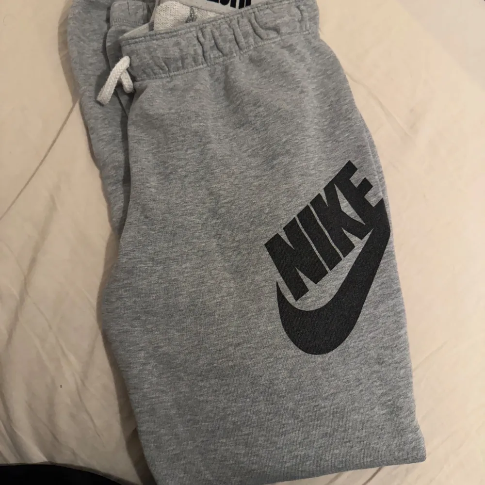 Säljer ett par grå mjukisbyxor från Nike i bra skick. De har en elastisk midja med snörning och ett stort Nike-logotyptryck på benet. Perfekta för en avslappnad dag eller träning. Superbekväma och stilrena! . Jeans & Byxor.