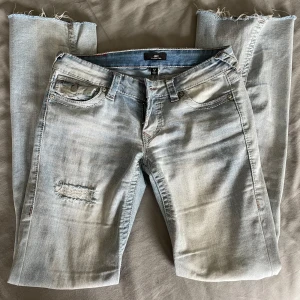 Ljusblå jeans, True Religion - Säljer ett par ljusblå jeans från True Religion i bra skick. De har en snygg bootcut-stil och är dekorerade med slitningar på framsidan.