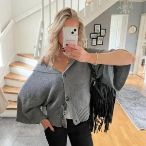 Grå kofta med knappar - Säljer en superfin grå kofta med stora knappar framtill. Den har en loose passform och trekvartsärmar, perfekt för en avslappnad look. Koftan är i mycket bra skick och passar perfekt till både vardag och fest. Den är gjord i ett mjukt material som känns skönt mot huden.