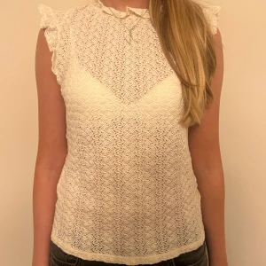 Vit spetsblus - Säljer en söt vit spetsblus med volangdetaljer vid ärmarna. Blusen är ärmlös och har en fin struktur som ger en romantisk känsla. Perfekt för sommarens alla tillfällen! 🕊️