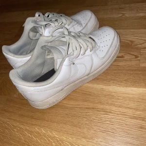Vita Nike Air Force sneakers - Säljer ett par klassiska vita Nike Air Force sneakers i bra skick. De har en stilren design med snörning och perforerade detaljer på tån för extra ventilation. Perfekta för både vardag och fest! Erbjuder att tvätta dom ifall de är ett måste men dom är vita.