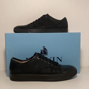 Svarta sneakers från Lanvin - Säljer ett par stilrena svarta sneakers från Lanvin då dem inte passar. Dem är knappt använda 9/10 skick.                (med endast en liten difekt vid tån). Säljer för 1799kr ny pris 5000 kr. Låda ingår i köp, skriv vid fler frågor.