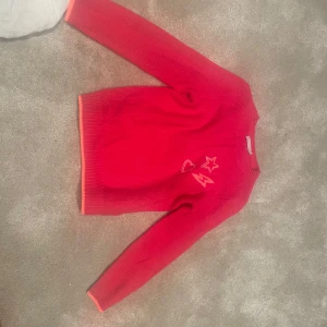 Röd stickad tröja från Mintie by london - Säljer en superfin röd stickad tröja från Mintie by london. Den har coola broderade detaljer med en stjärna, ett hjärta och en blixt på framsidan. Tröjan är långärmad och perfekt för höst och vinter. Den är i bra skick och redo för nya äventyr! 🌟❤️⚡