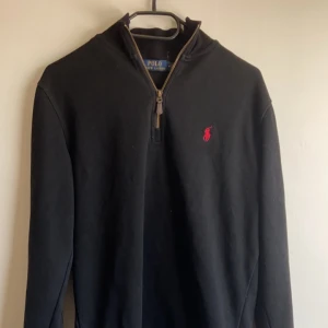 Ralph lauren zip  - Säljer en stilren svart tröja från Polo Ralph Lauren med en halv dragkedja och det klassiska röda logotypen på bröstet. Perfekt för både vardag och lite finare tillfällen. Tröjan har långa ärmar och är i mycket bra skick. Passar perfekt till höst och vinter!