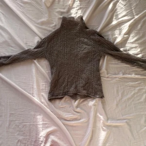 Grå stickad polotröja från Amomento - Säljer en supermysig grå stickad polotröja från Amomento. Den är i storlek S och har ett snyggt kabelstickat mönster. Tröjan är gjord av en blandning av  alpacka, ull, nylon och akryl. Passar perfekt till både vardag och lite finare tillfällen. Obs. Att det finns ett litet hål på ryggen