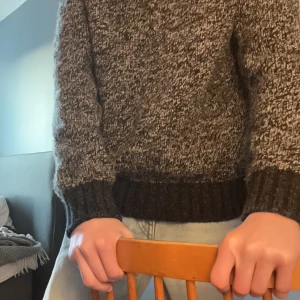  stickad tröja - Säljer en mysig melerad stickad tröja i grått och svart. Perfekt för kyliga dagar med sin varma och bekväma passform. Tröjan har långa ärmar och ribbade muddar vid ärmslut och nederkant. Passar både till vardags och lite finare tillfällen.