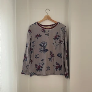 Blommig långärmad tröja från edc - Säljer en superfin blommig tröja från edc i storlek XS. Den har en ljus bas med blommönster i blått och rött. Tröjan är långärmad och har en randig krage i rött, svart och vitt. Perfekt för både vår och höst!
