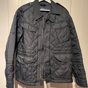 Svart quiltad jacka från Polo Ralph Lauren - Säljer en snygg svart quiltad jacka från Polo Ralph Lauren i storlek M. Jackan har en dragkedja och knappar framtill, samt flera praktiska fickor. Äldre modell men knappt använd, nypris 4000:-