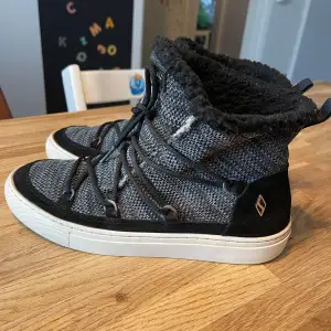 Säljer ett par snygga och bekväma sneakers från Skechers i grått och svart. De har en stickad yta med snörning och en mysig fleecefodring som håller fötterna varma. Perfekta för höst och vinter! Sulan är vit och ger en cool kontrast till resten av skon. Använda ett fåtal gånger men i mycket bra skick.