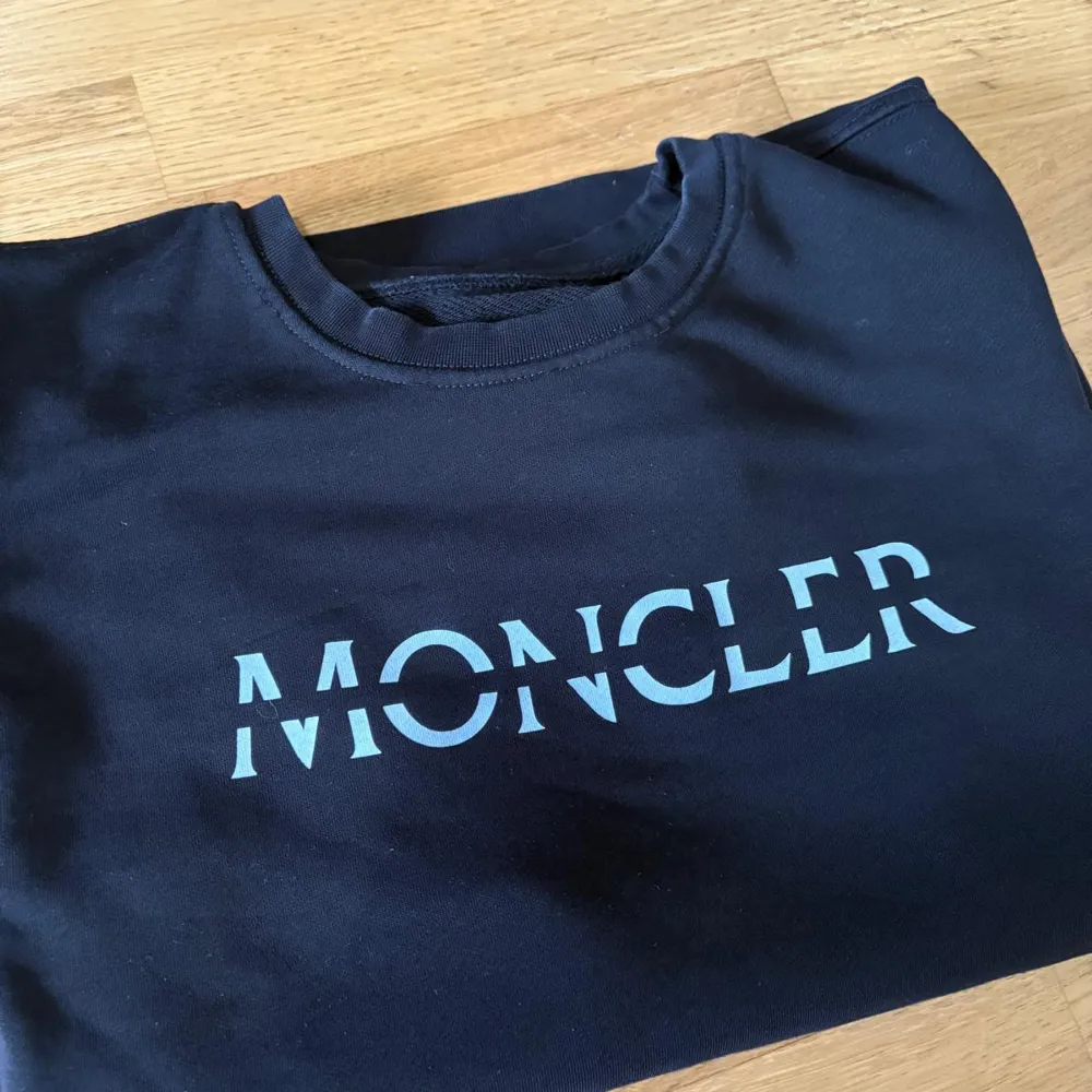 Säljer en stilren svart sweatshirt från Moncler. Den har en klassisk rund halsringning och Moncler-loggan tryckt i vitt på bröstet. Perfekt för både vardag och avslappnade tillfällen. Passar bra till jeans eller joggers för en casual look.. Tröjor & Koftor.