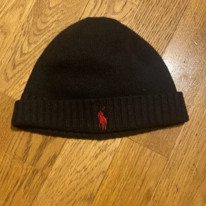 Ralph lauren mössa - Svart ralph lauren mössa med rött polomärke. Liten i storleken. Använd ett fåtal gånger. Perfekt nu till kallare tider. Skriv vid intresse/frågor.